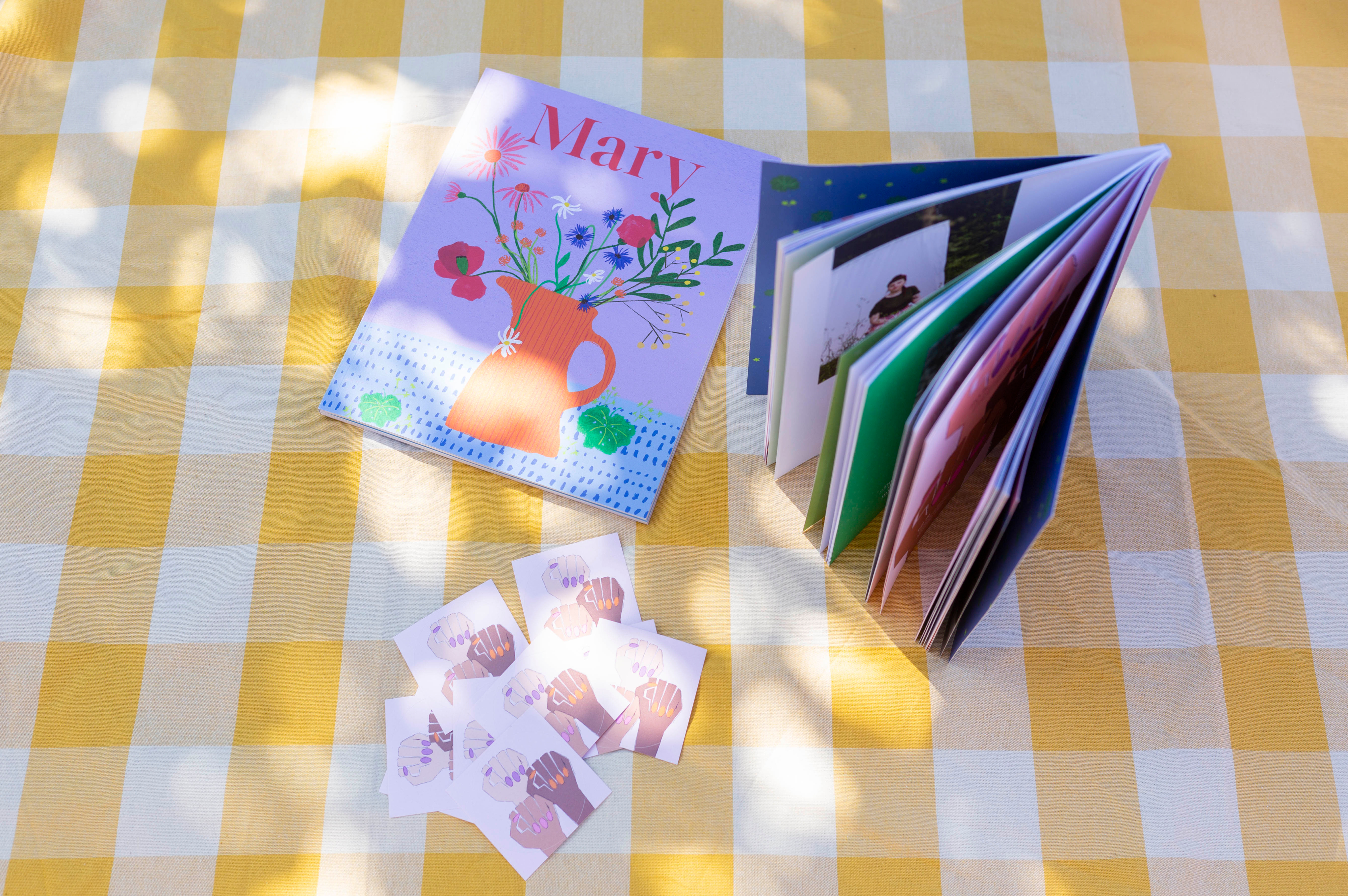 Zeitschrift, Postkarten und Sticker auf gelber Picknickdecke platziert