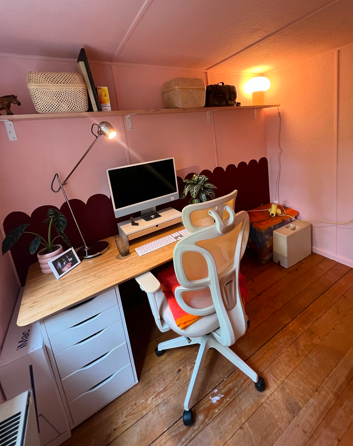 Atelier-Raum der Designerin mit pink-roten Wänden, Schreibtisch, Stuhl und Pflanzen, warmes Licht